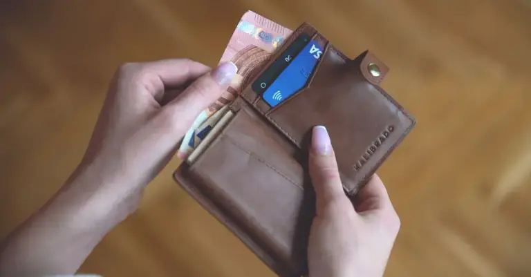 Mãos abrindo carteira com cartão de crédito e notas de dinheiro