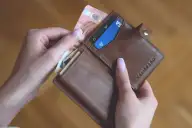 Mãos abrindo carteira com cartão de crédito e notas de dinheiro