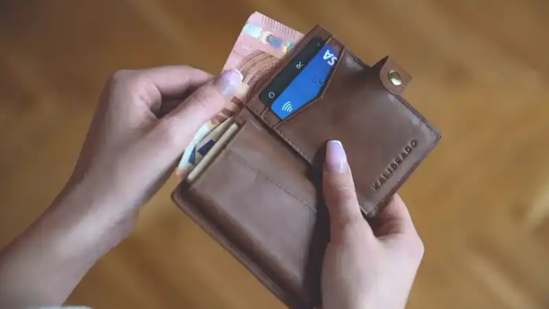 Mãos abrindo carteira com cartão de crédito e notas de dinheiro