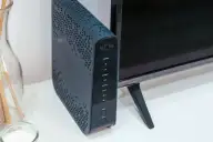 Roteador Wi-Fi sobre móvel na sala, ao lado de uma televisão e de objetos decorativos