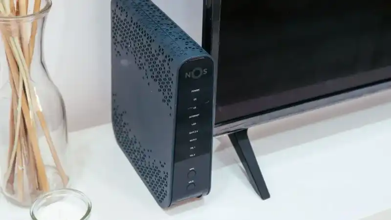 Roteador Wi-Fi sobre móvel na sala, ao lado de uma televisão e de objetos decorativos