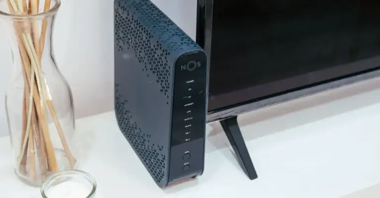 Roteador Wi-Fi sobre móvel na sala, ao lado de uma televisão e de objetos decorativos