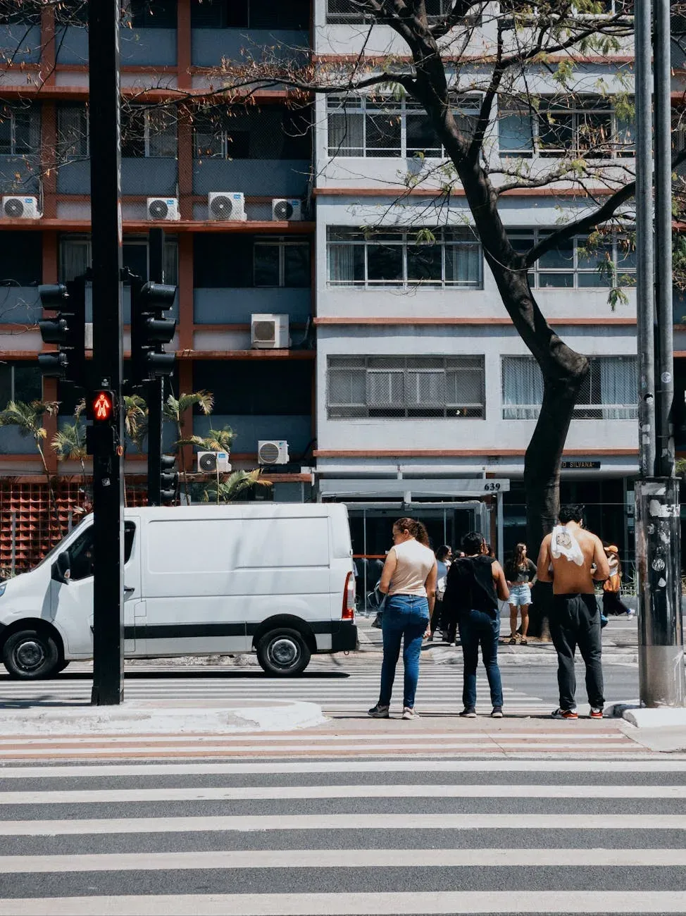 Pessoas atravessando uma rua em São Paulo durante o dia, com a arquitetura urbana ao fundo.