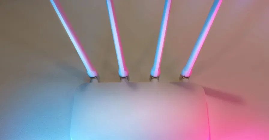 Roteador Wi-Fi branco com quatro antenas externas, iluminado por luz rosa e azul