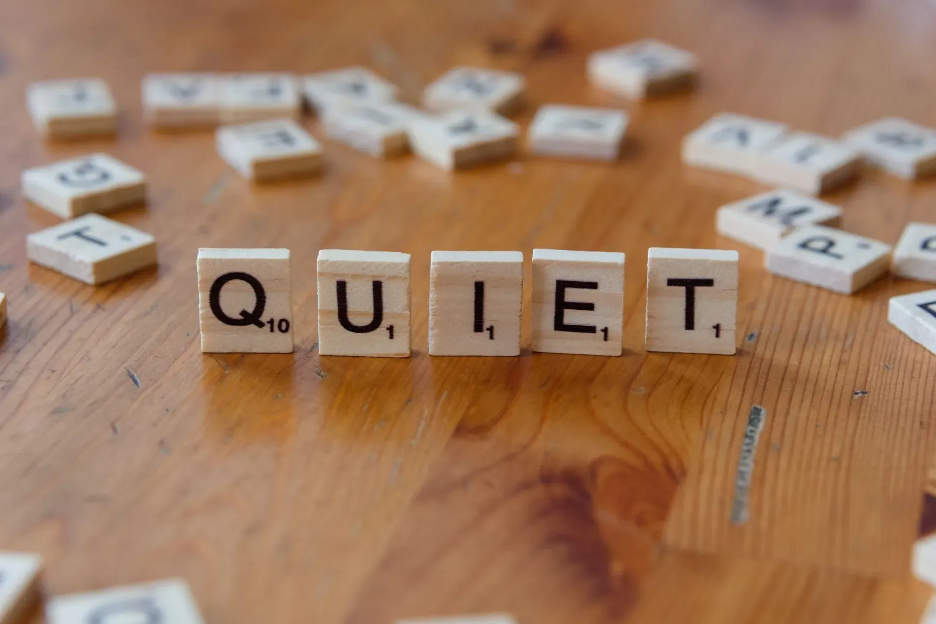Peças de Scrabble com a palavra 'QUIET' escrita em uma superfície de madeira, simbolizando calma e tranquilidade.